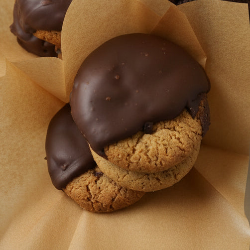 Three chocolate-dipped cookies on brown paper against a light background
