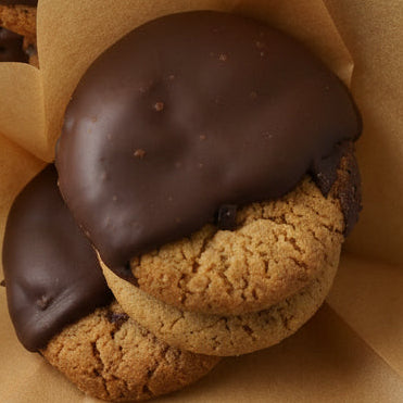Three chocolate-dipped cookies on brown paper against a light background